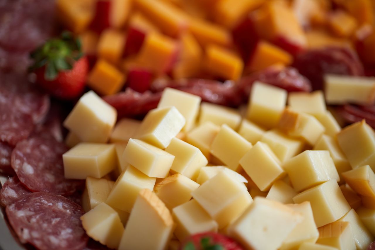 Close-up of assorted cheeses and salami on a gourmet platter with strawberries.