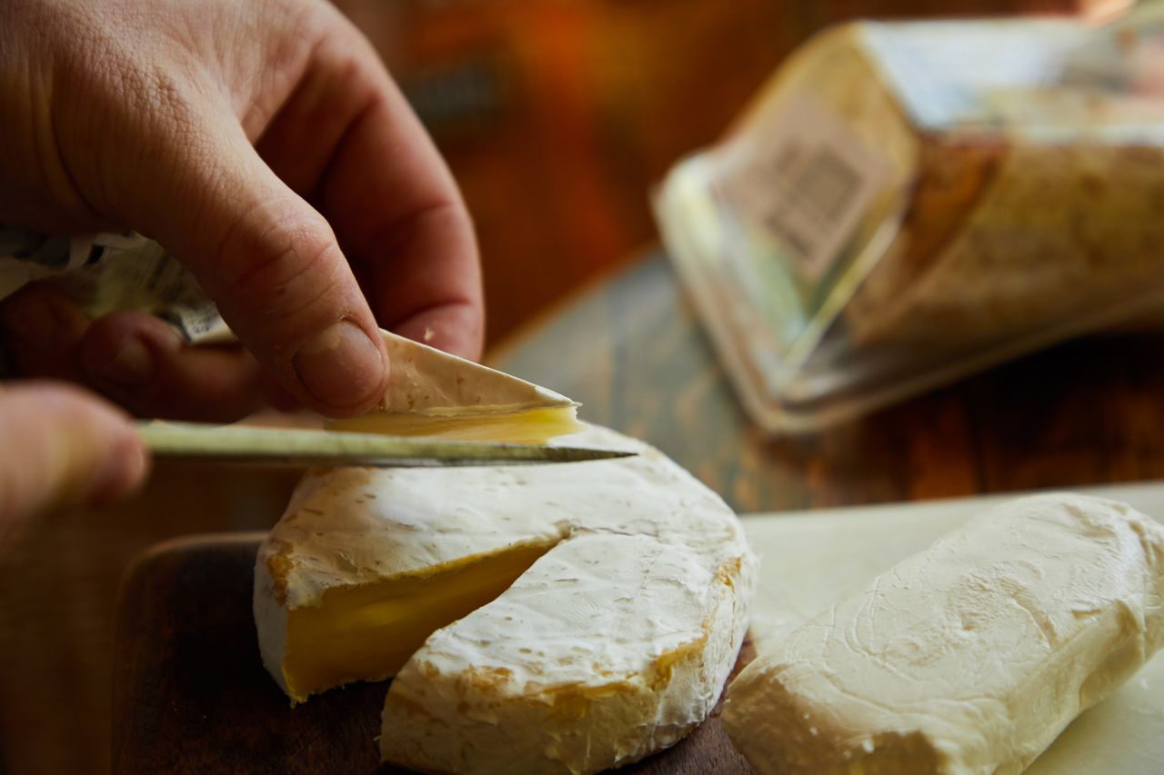 A close-up of hands slicing creamy Brie cheese on a wooden board. Perfect food photography.